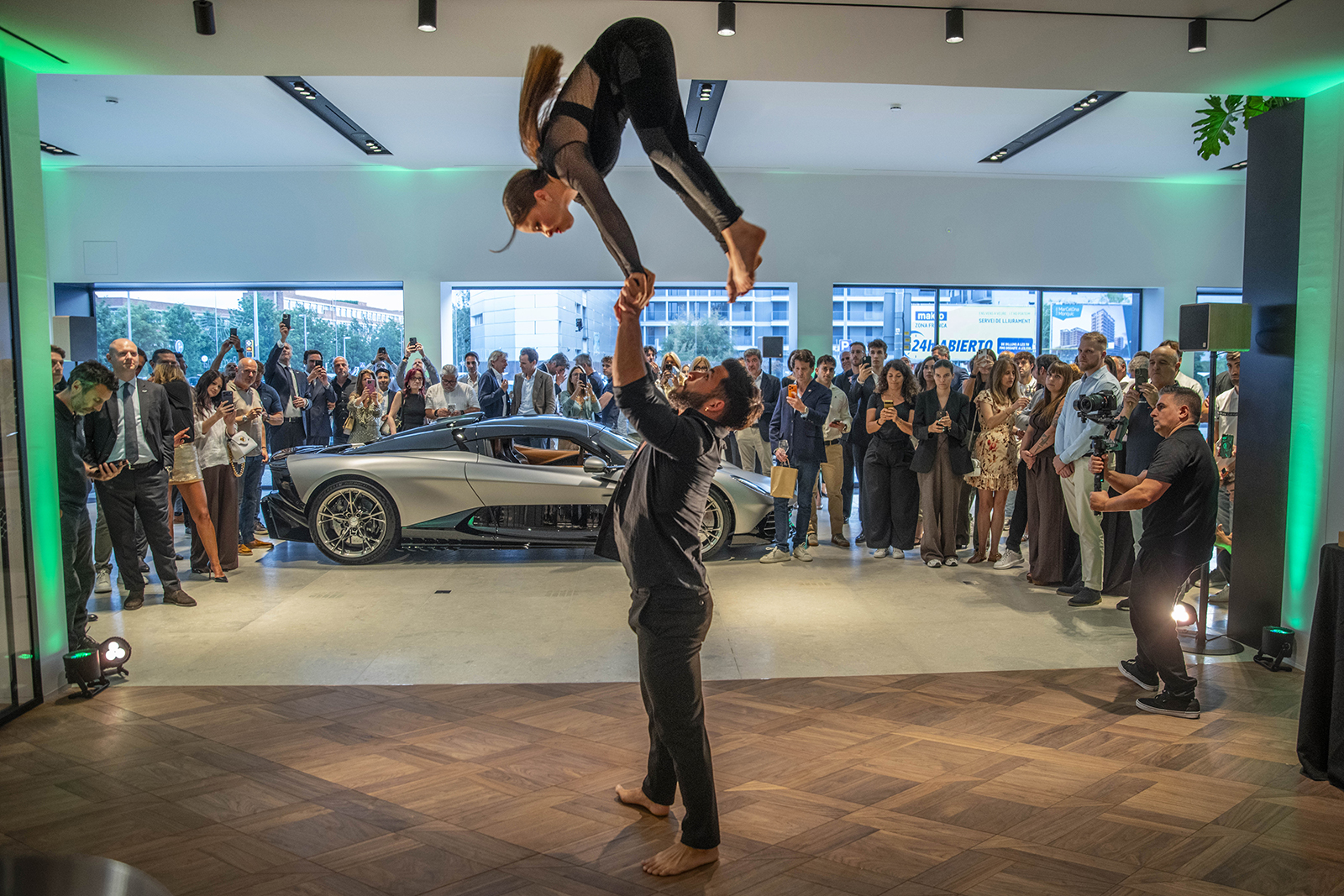 Espectáculo de acróbatas de equilibrio mano a mano en la inauguración del concesionario Aston Martin en Barcelona, con público VIP y un Aston Martin de fondo